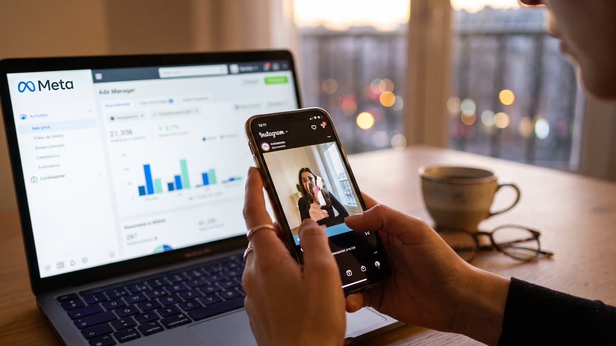 Une main tient un téléphone qui diffuse une publicité vidéo dans Instagram, devant un ordinateur ouvert sur le gestionnaire de publicités Meta